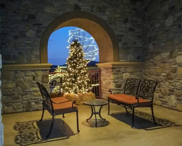 A covered sitting area decorated for the holidays, with a lit Christmas tree under a stone arch